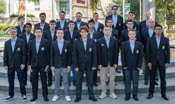 Roster photo of the UT Dallas chess team, standing in front of the UT Dallas Fountain, wearing their chess coats.