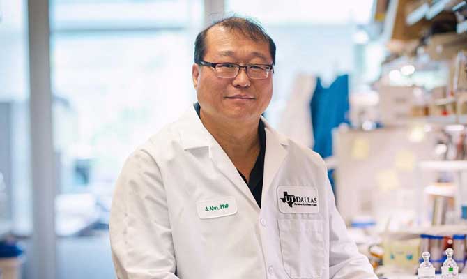 Dr. Jung-Mo Ahn, associate professor of chemistry and biochemistry at UT Dallas, sitting in a lab next to a counter of medicine vials