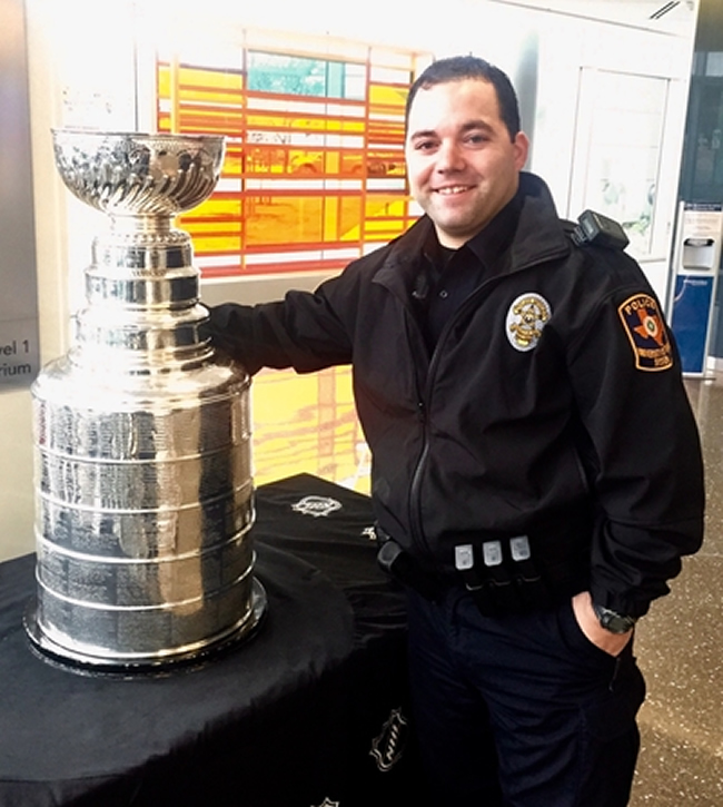 Officer Slott, smiling in his uniform, stands next to a large, silver trophy.