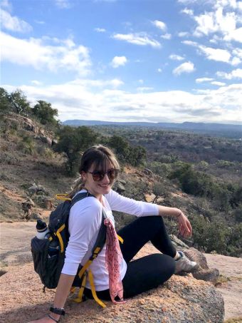 Grace sitting down on a large rock during a hike, with a beautiful Texas landscape behind her