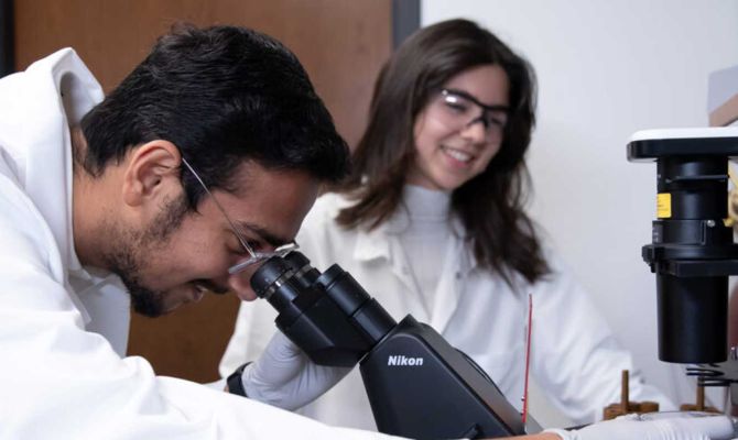 Two researchers in a lab, looking through a micoscrope