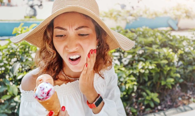 A woman holds her hand to her mouth in pain, from a freeze pain reaction from eating ice cream.