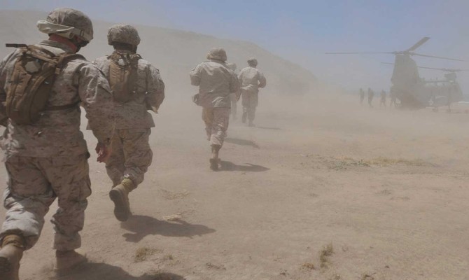 Marines move through a dust cloud toward a CH-46 Sea Knight Helicopter