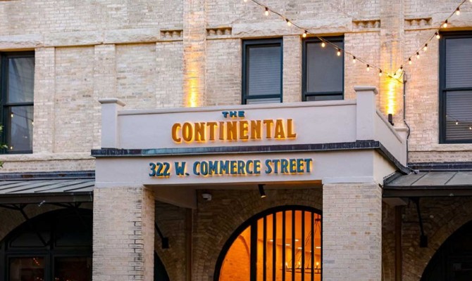 Historic beige brick building facade with illuminated sign reading "The Continental" at 322 W. Commerce Street, strung with warm yellow lights.