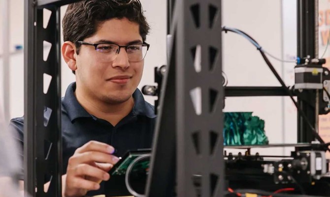 A UT San Antonio engineering student makes adjustments to a 3D printer in the university's Makerspace.