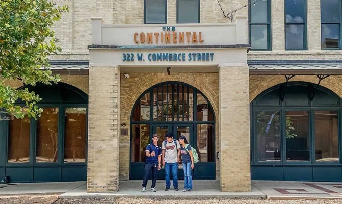 Historic brick storefront of The Continental at 322 W. Commerce Street, with three people posing beneath its arched entrance.