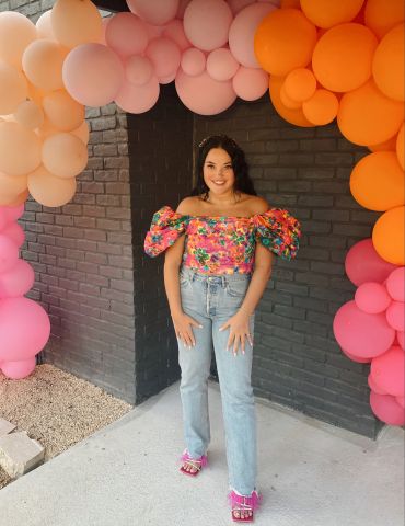 Taylor Naiser, purchasing coordinator for UT System's Office of Contracts and Procurement is standing under an arch of orange and pick balloons.