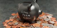 A piggy bank with the text: "Long term care" written on the side, and the standing on a pile of pennies, nickels and dimes. 