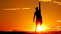 Image of a person in front of a sunset raise their arm and fist in triumph
